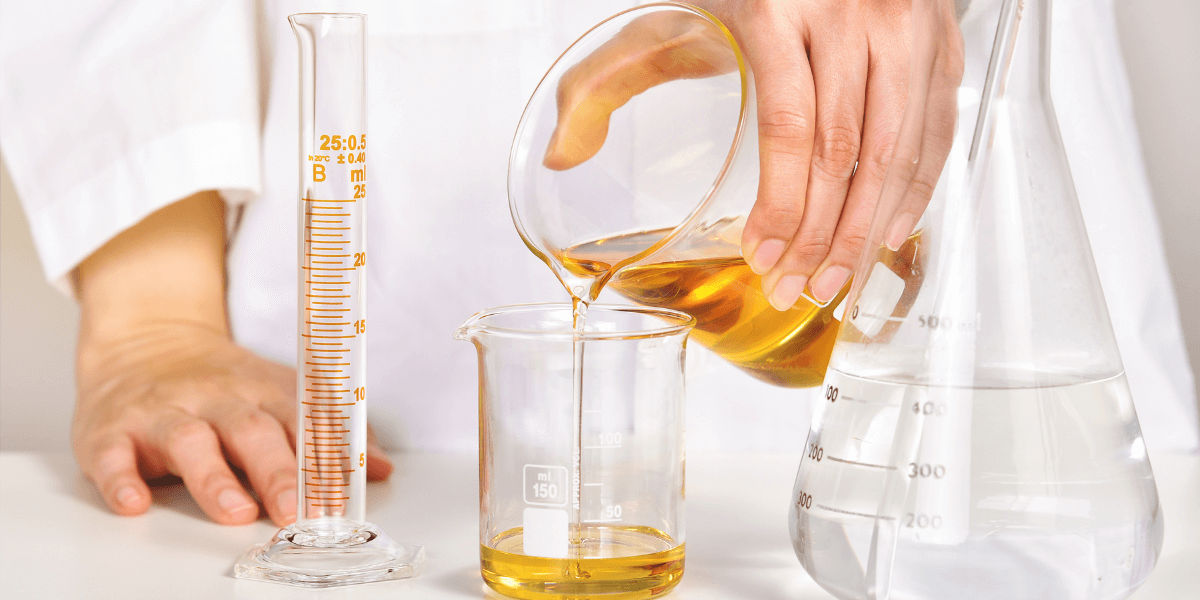 Hand pouring yellow liquid into a beaker in a lab
