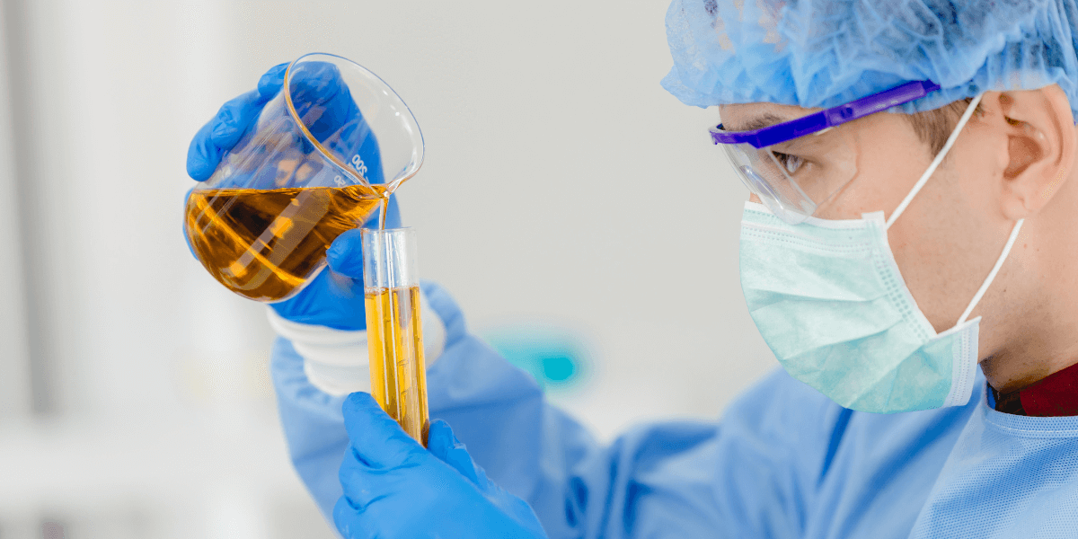 Scientist pours yellow liquid into a test tube in a lab.